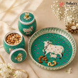 A set of decorative ceramic baking jars and a serving platter in teal green with white cow illustrations, shown on a beige fabric background with flowers and nuts as props. The Bakeyy brand logo is visible in the top right corner.