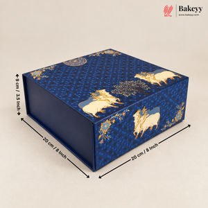 A rectangular blue bakery gift box with a patterned design featuring cream-colored cows and gold decorative motifs, shown with dimension arrows indicating measurements of 20 cm by 20 cm by 8 cm on a light beige background. The Bakeyy logo is visible in the top right corner.