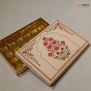 An ornate rectangular gift box with a cream-colored lid decorated with a pink floral arch motif and green leaves, shown next to an open box revealing gold foil compartments inside, on a neutral gray background.