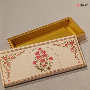 An ornate rectangular gift box with a cream-colored exterior decorated with pink floral motifs and gold borders, shown open with a shiny gold interior. A small Bakeyy watermark is visible in the top right corner.