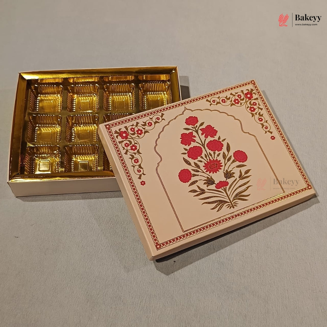 An open decorative gift box containing 12 individually wrapped chocolates, with the lid leaning against the box. The box has a gold interior tray and a cream-colored exterior lid decorated with red floral motifs and brown detailing, set on a neutral gray background.