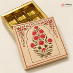An open gold-colored rectangular box with six compartments, shown next to its illustrated cream lid featuring red flowers and green leaves, on a light beige background. A Bakeyy logo is visible in the top right corner.