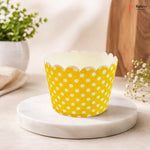 Yellow cupcake liner with white polka dots on a marble surface.