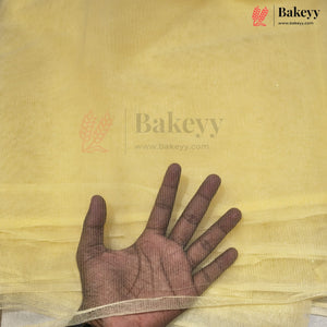 A hand is placed underneath a sheet of pale yellow chiffon fabric to show its texture and transparency. The Bakeyy brand logo is visible in the top right corner.
