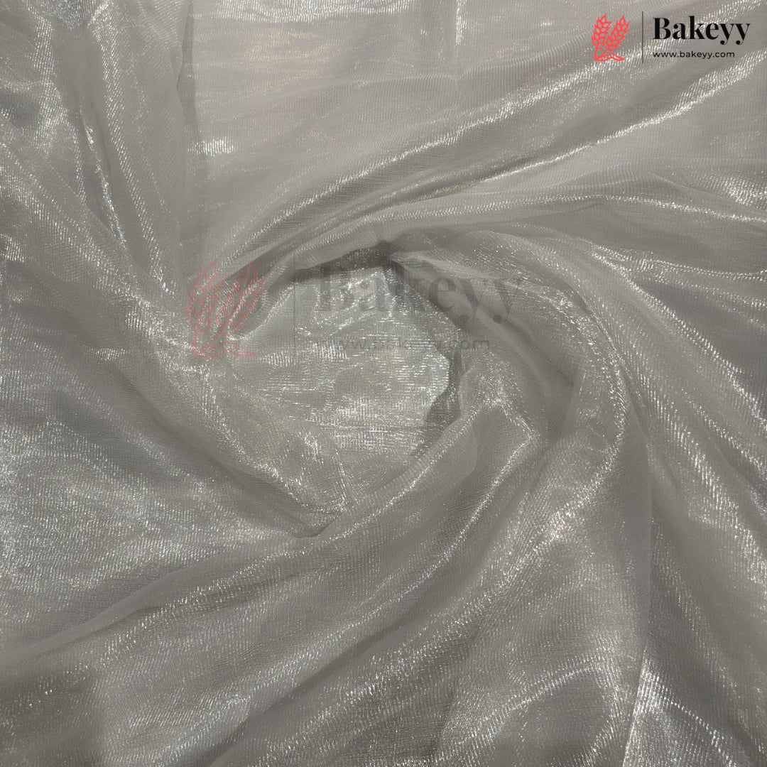 Shimmering silver organza fabric with a metallic reflective finish, draped in a swirl pattern. A Bakeyy brand logo is visible in the top right corner.