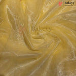 Yellow sheer mesh fabric with a subtle metallic sheen, swirled and draped to show its texture and transparency. A Bakeyy brand logo is visible in the top right corner.