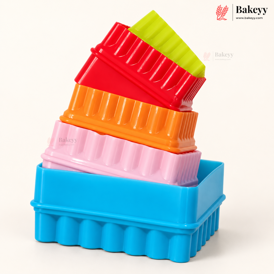 A stack of five colorful rectangular baking molds or trays with fluted edges, shown on a clean white background. The colors from bottom to top are blue, pink, orange, red, and lime green.