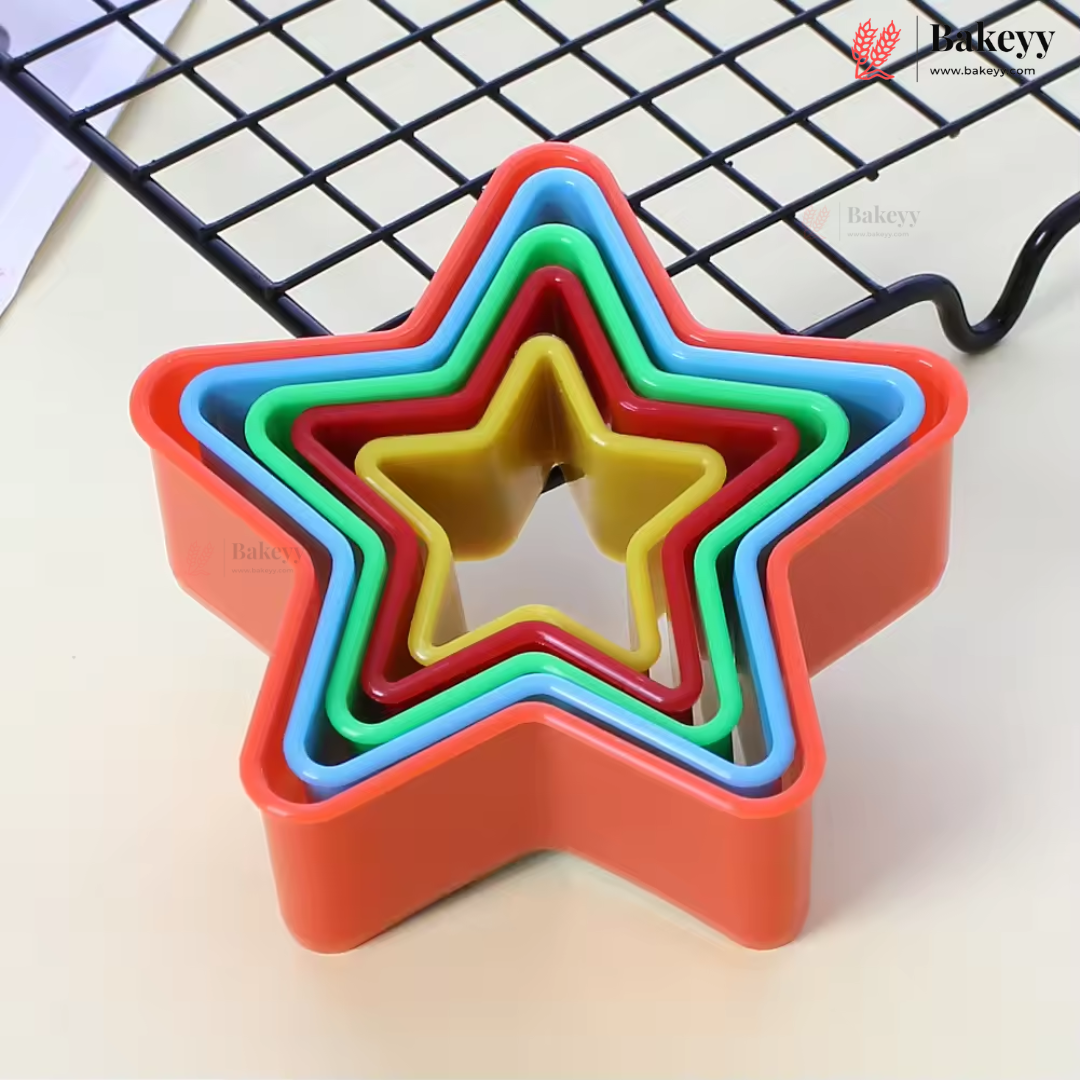 A set of five nested star-shaped cookie cutters in bright colors including orange, blue, green, red, and yellow, arranged on a light beige surface with a black wire cooling rack in the background.