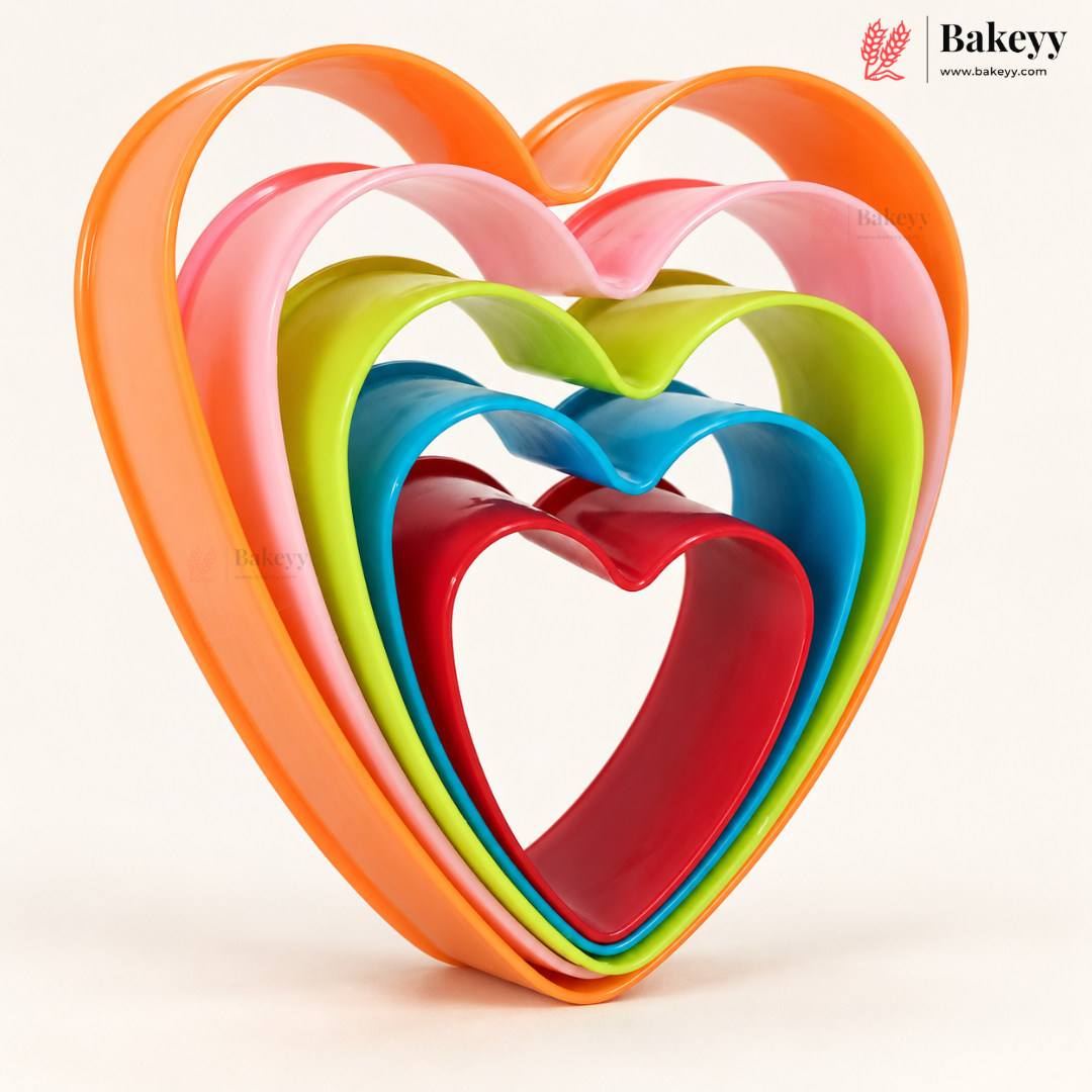 A set of nested heart-shaped cookie cutters in bright colors including orange, pink, green, blue, and red, displayed on a clean off-white background with the Bakeyy brand logo in the top right corner.