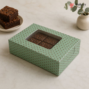 Green polka dot box with brownies on a light surface, featuring a plant in the background.