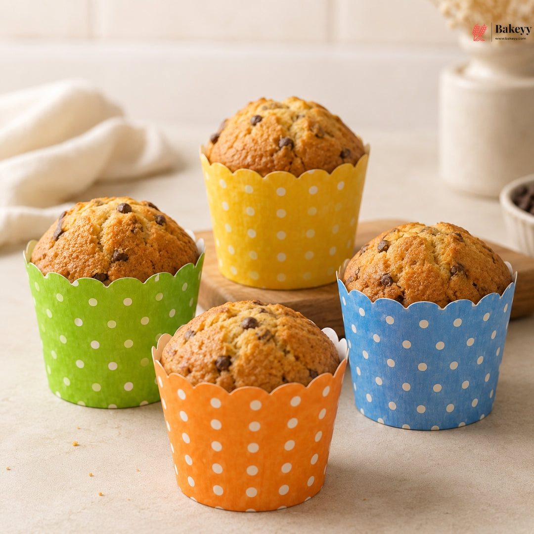 Four muffins in colorful polka dot paper cups on a light surface.