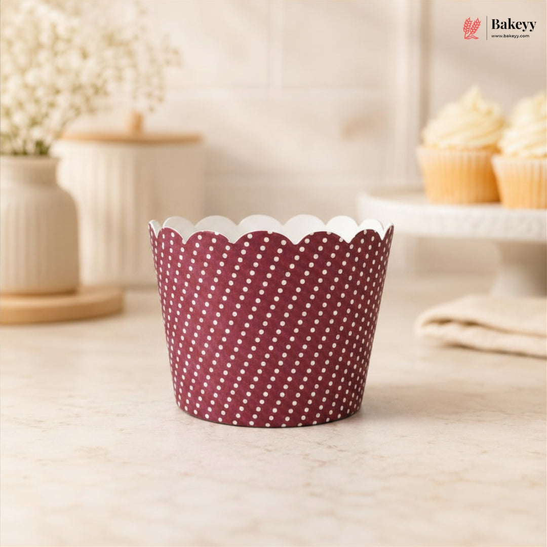 Maroon cupcake liner with white polka dots on a light wooden surface, with 'Bakeyy' branding in the background.