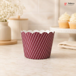Maroon cupcake liner with white polka dots on a light wooden surface, with 'Bakeyy' branding in the background.