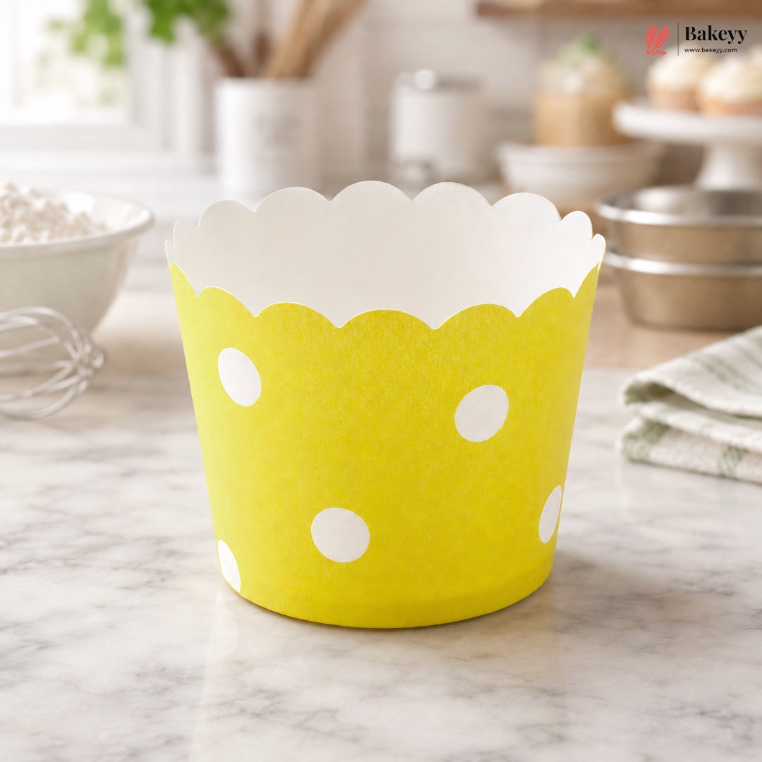 Yellow cupcake liner with white polka dots on a marble surface, branded 'Bakeyy'.