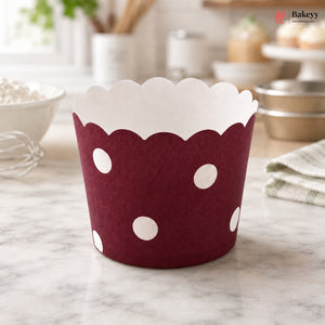 Red muffin cup with white polka dots on a marble surface, branded 'Bakeyy'.