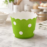 Green cupcake liner with white polka dots on a marble surface, branded 'Bakeyy'.