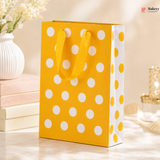 Yellow gift bag with white polka dots on a light wooden surface