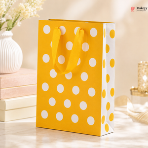 Yellow gift bag with white polka dots on a light wooden surface