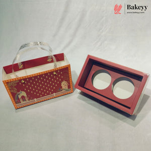 A red and orange bakery gift box set with a decorative printed exterior and a matching interior tray featuring two circular cutouts, photographed on a light gray fabric backdrop. A Bakeyy logo watermark is visible in the top right corner.