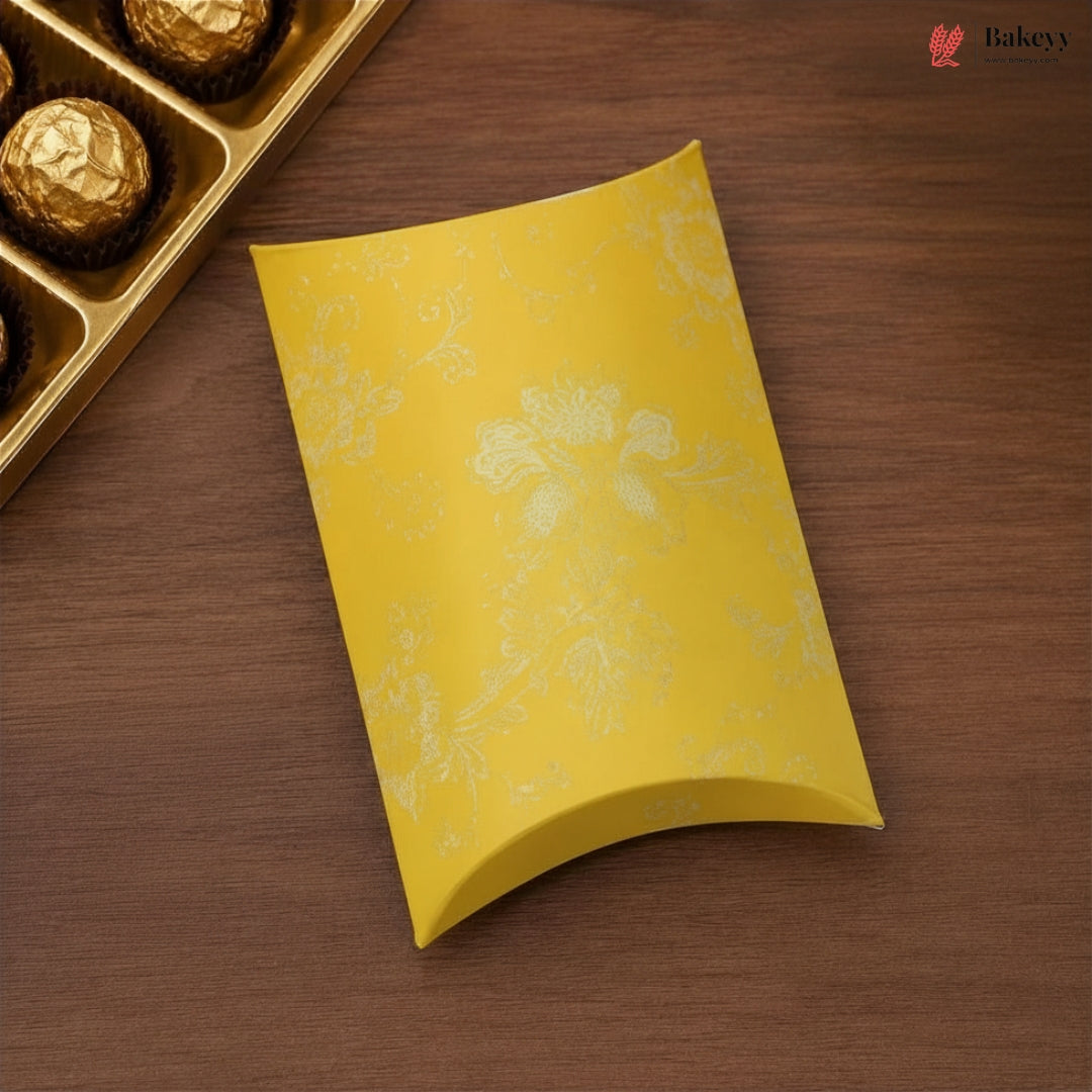 Yellow decorative box on a wooden surface with a gold tray of chocolates.