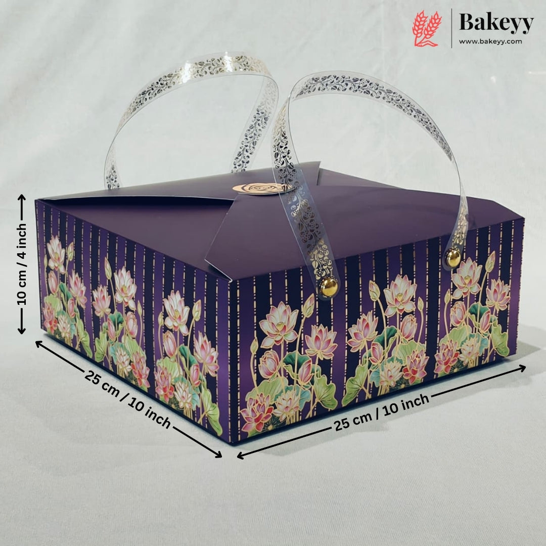 A rectangular purple bakery gift box with floral print on the sides, featuring two clear handles with silver glitter trim and gold-tone clasps. Black dimension lines and text indicate measurements of 25 cm x 25 cm x 10 cm.