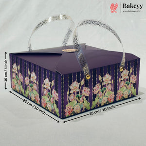 A rectangular purple bakery gift box with floral print on the sides, featuring two clear handles with silver glitter trim and gold-tone clasps. Black dimension lines and text indicate measurements of 25 cm x 25 cm x 10 cm.
