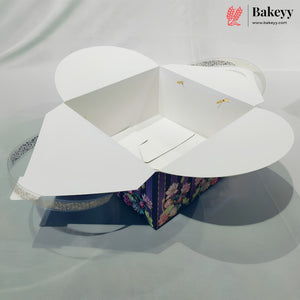 A white bakery gift box with flared lid wings, shown open and empty on a light gray fabric background. A smaller floral-patterned box is partially visible underneath, and a Bakeey logo watermark appears in the top right corner.