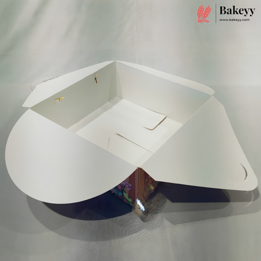 A white cardboard bakery box with flared sides and a triangular base, shown open on a light gray fabric background. The Bakeyy logo is visible in the top right corner.
