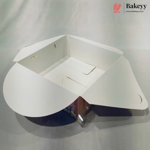 A white cardboard bakery box with flared sides and a triangular base, shown open on a light gray fabric background. The Bakeyy logo is visible in the top right corner.