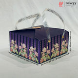 A rectangular bakery gift box with a dark purple lid and floral-patterned sides, shown on a light fabric background with dimension arrows and text indicating 20 cm by 20 cm and 10 cm height. A Bakeyy logo appears in the top right corner.