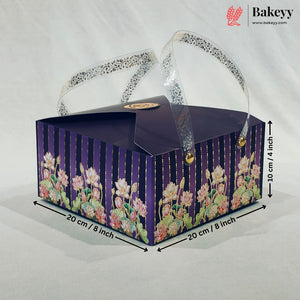 A rectangular bakery gift box with a dark purple lid and floral-patterned sides, shown on a light fabric background with dimension arrows and text indicating 20 cm by 20 cm and 10 cm height. A Bakeyy logo appears in the top right corner.