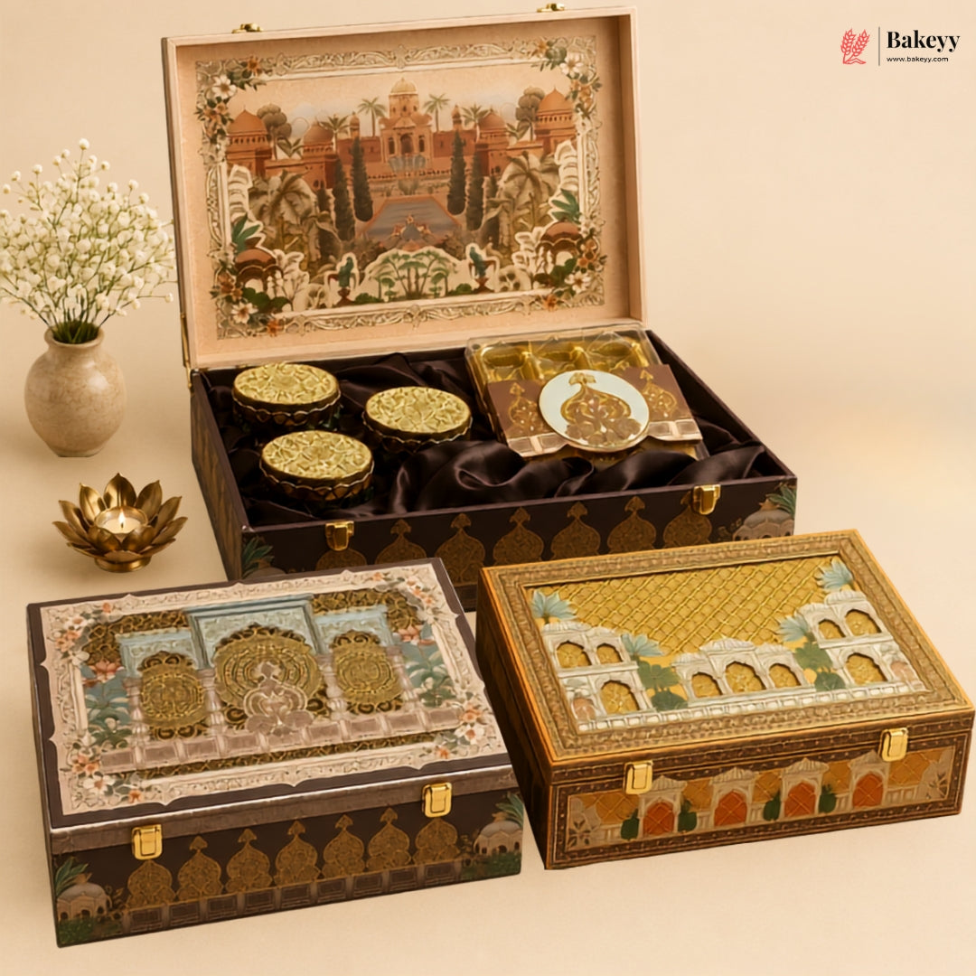 Three ornate decorative gift boxes with intricate architectural illustrations and gold detailing, arranged on a beige background. One box is open, showing round gold-lidded containers inside a black velvet-lined compartment.