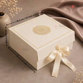 A cream-colored rectangular gift box with a gold mandala design on the lid, decorated with a cream satin ribbon bow. Black dimension lines with text indicate the box's measurements: 25.