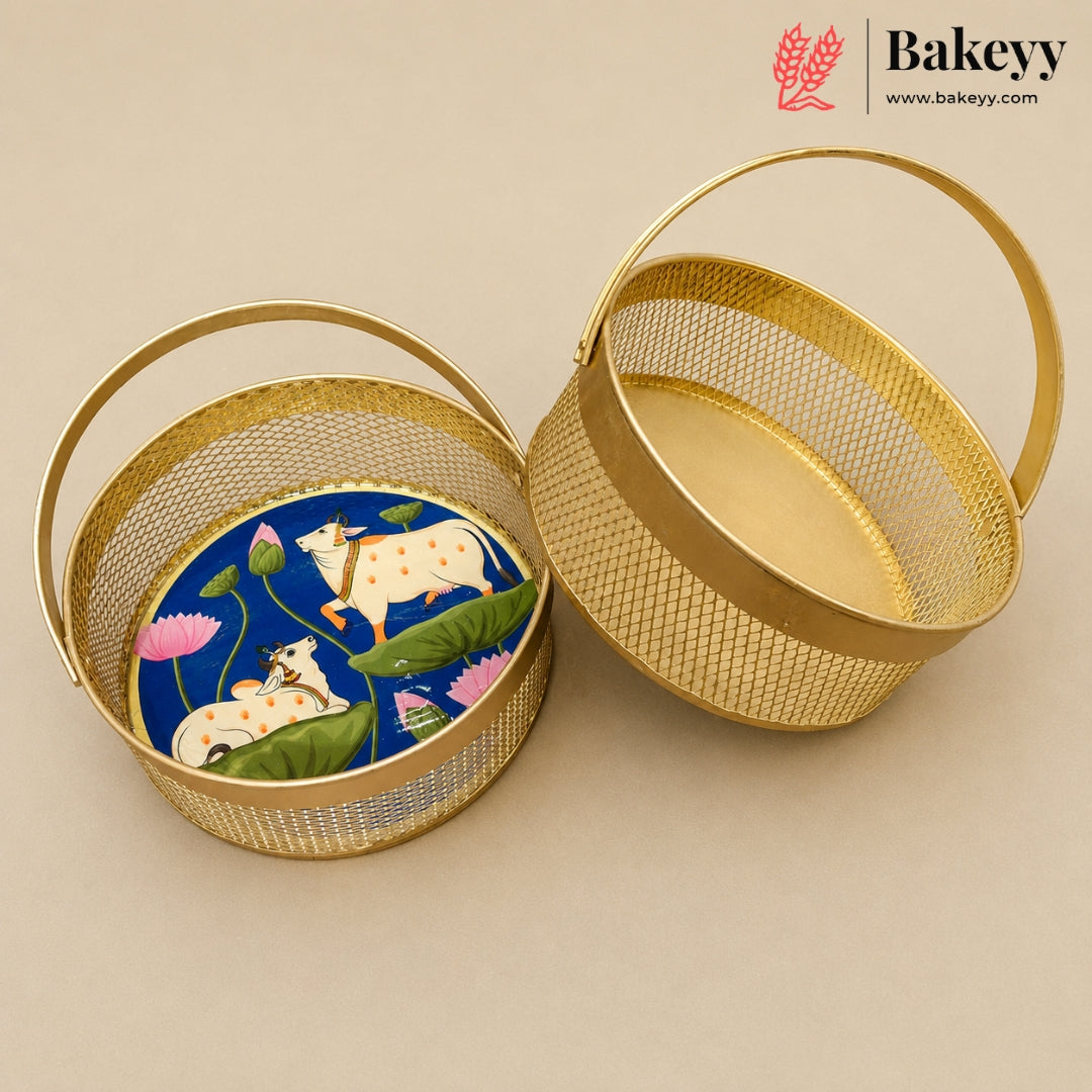 Two round gold metal baskets with mesh sides and top handles, shown on a beige background. One basket is open and displays a colorful printed insert featuring cows, lotus flowers, and green leaves on a blue background.