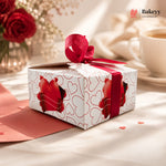 Gift box with red ribbon and heart designs on a table with flowers and a cup in the background, featuring the Bakeyy brand.