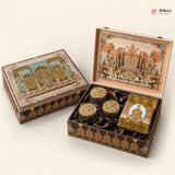An ornate traditional Indian gift box set shown closed and open on a light beige background. The set includes a large decorated box with a detailed architectural illustration on the lid, three small round gold-lidded jars, and a square wrapped item.
