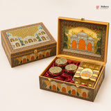 An ornate decorative gift box for sweets, shown closed and open on a light beige background. The box features intricate hand-painted architectural designs in gold, orange, and green, lined with red velvet inside.