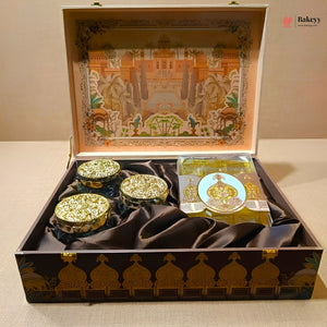 An ornate open gift box containing three small round decorative jars with gold lids and a packaged item, set on a beige surface. The box has a dark brown exterior with gold architectural detailing, and the interior lid features a colorful illustrated scene.