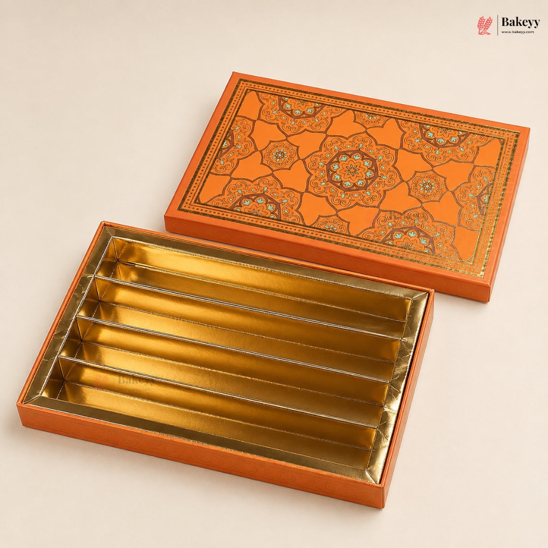 An open rectangular gift box with five compartments lined in metallic gold, shown with its matching lid placed behind it on a light beige background. The lid features an intricate orange and gold geometric floral pattern.