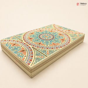 An ornate rectangular cake box with a detailed geometric and floral mandala pattern in teal, orange, red, and cream, shown on a solid light beige background. The Bakeyy logo is visible in the top right corner.