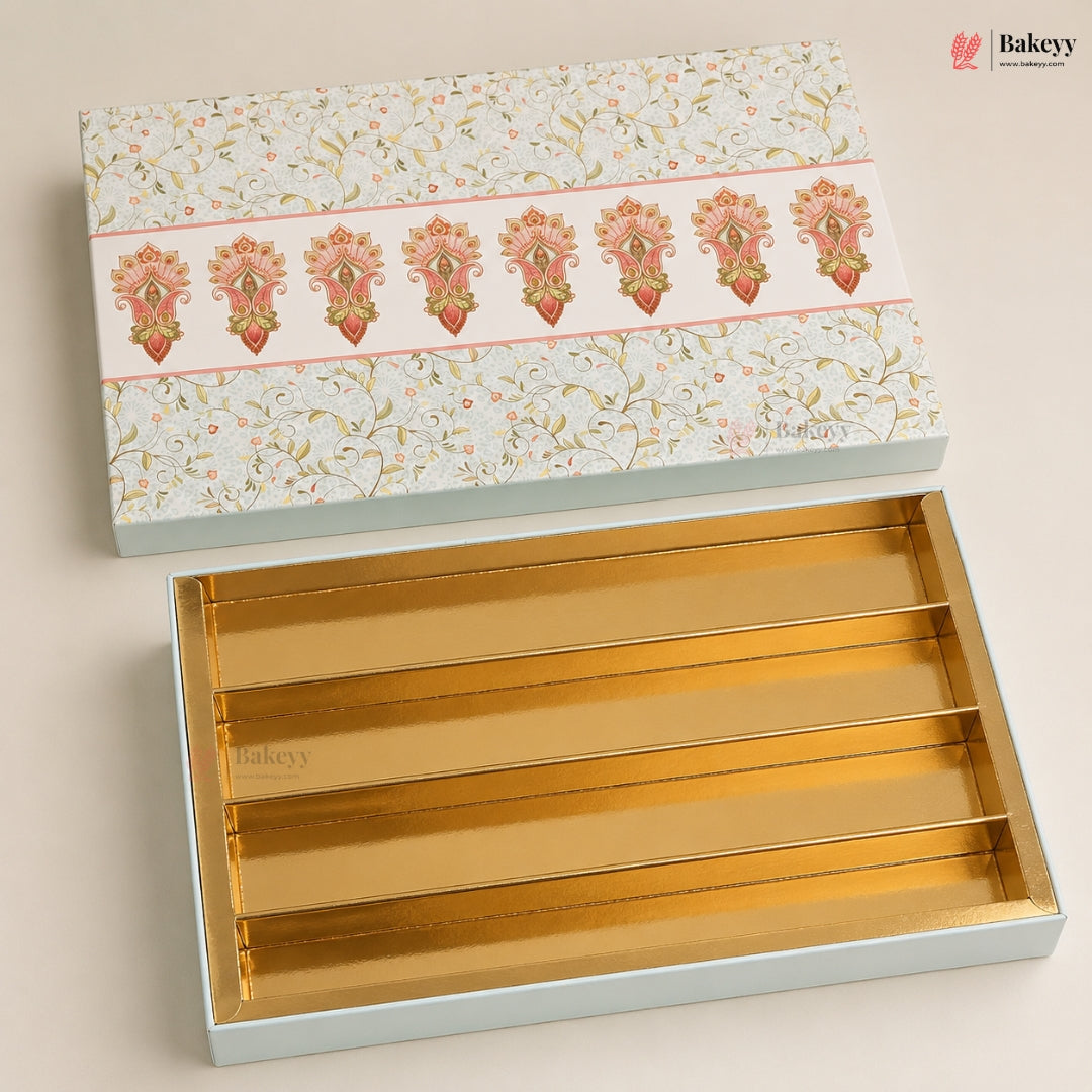 An open rectangular bakery gift box with a floral-patterned lid and gold interior trays, photographed on a light beige background. The Bakeyy logo appears in the top-right corner.