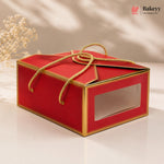 Red gift box with gold accents and a clear window on a beige background, featuring the Bakeyy brand.
