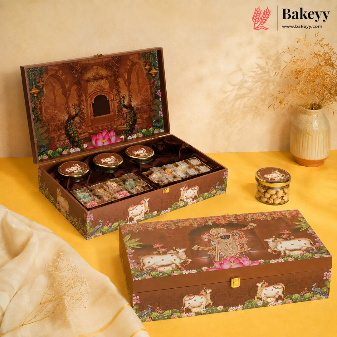 A decorative Bakeyy gift box set displayed on a yellow surface against a beige backdrop. The set includes an open box showing assorted packaged sweets and jars, plus a closed matching box in front.