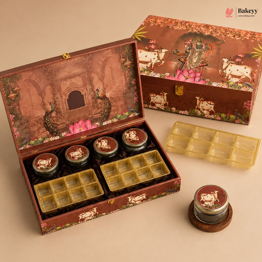 A decorative brown gift box set for sweets, shown open with several small round jars and yellow plastic tray inserts. The box lid features an illustrated temple scene with peacocks and pink lotus flowers, and the closed box in the background shows cows and floral motifs.