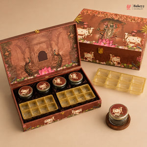 A decorative brown gift box set for sweets, shown open with several small round jars and yellow plastic tray inserts. The box lid features an illustrated temple scene with peacocks and pink lotus flowers, and the closed box in the background shows cows and floral motifs.