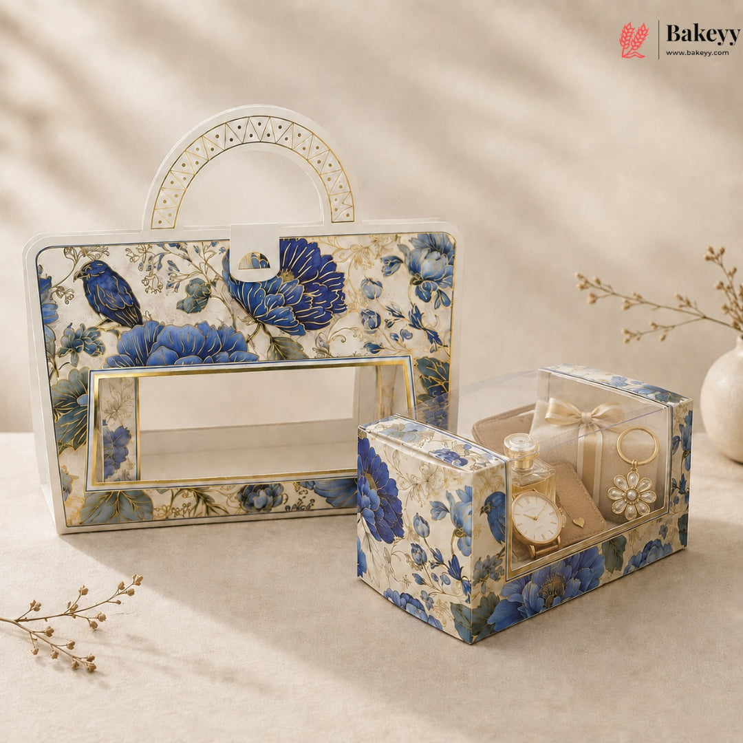 A decorative gift box set with a large rectangular carrying case and a smaller square presentation box, both covered in a blue floral and bird pattern with gold trim, styled on a beige surface with dried flowers and soft shadows.