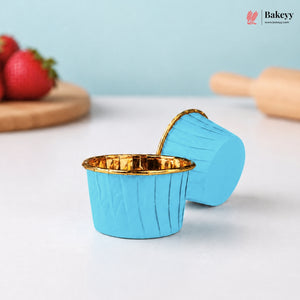 Blue silicone baking cup with gold interior on a white surface, surrounded by strawberries and a rolling pin.
