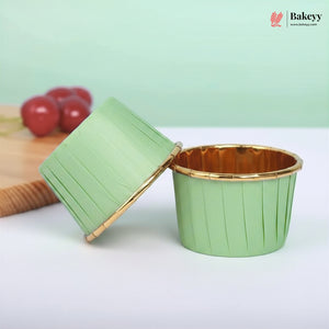 Green cupcake liner with gold rim on a white surface, branded 'Bakey'.