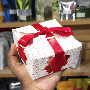 Gift box with red ribbon held by a hand, with blurred shelves in the background
