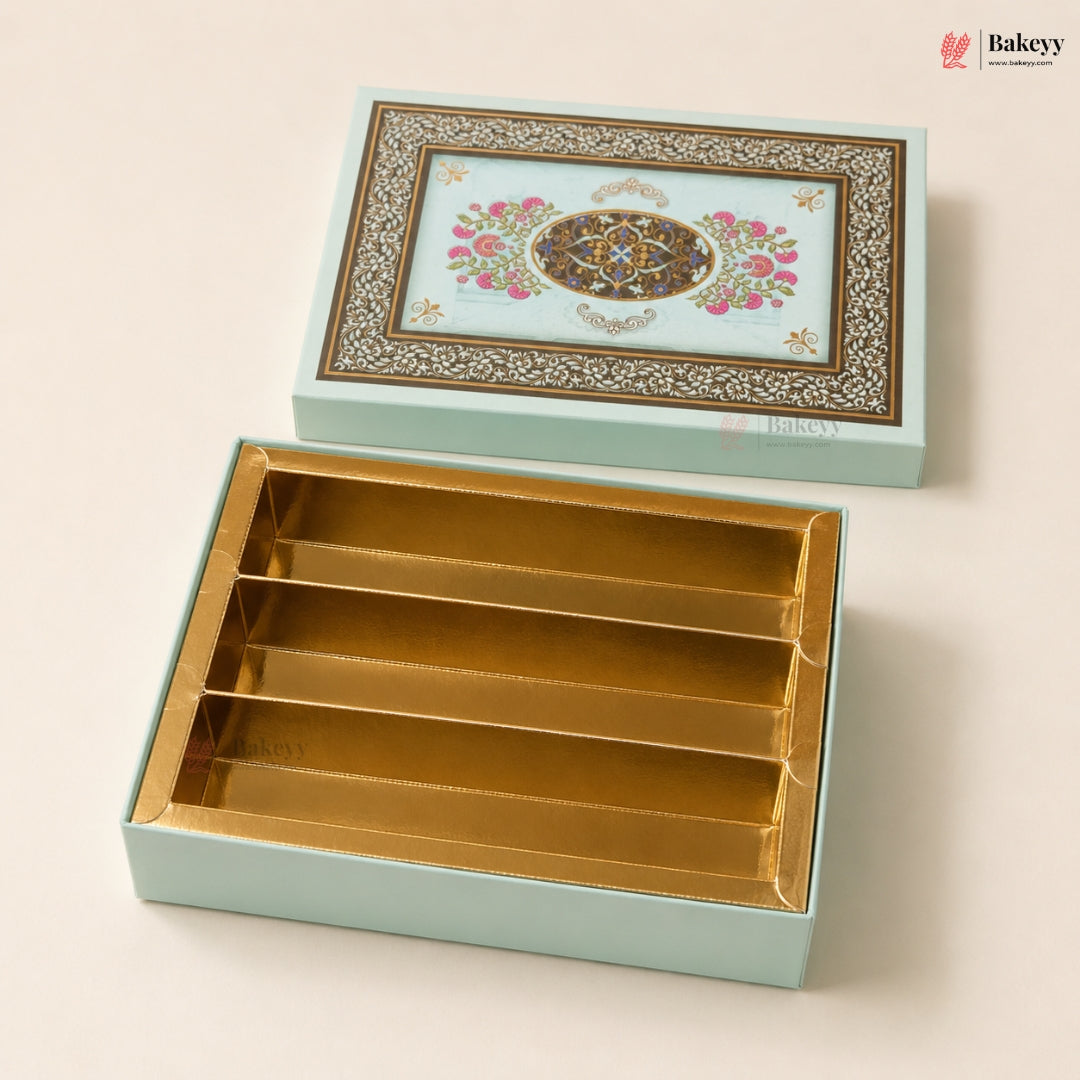 A decorative rectangular gift box set from Bakeyy, featuring a light aqua exterior with an ornate floral and geometric pattern on the lid, and a gold-foil lined interior with four compartments, shown open on a warm beige background.